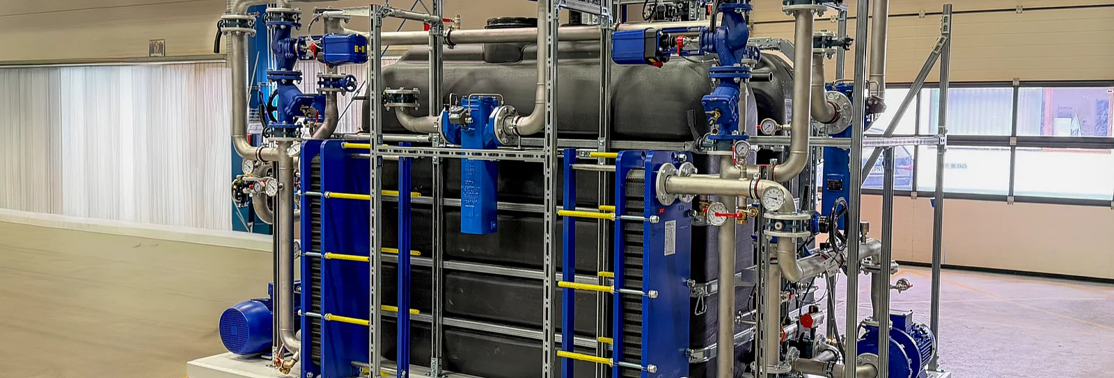Wärmerückgewinnungsanlage mit blauen Plattenwärmetauschern, Pumpen und Rohrleitungen in einer Werkhalle